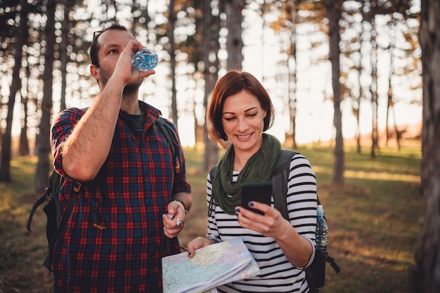 Hiking couple navigating in forest using map and smart phone