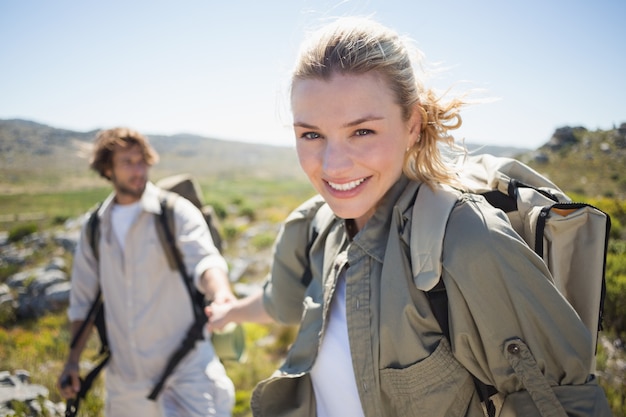 カメラで笑顔山の地形の女性の上に立つハイキングカップル