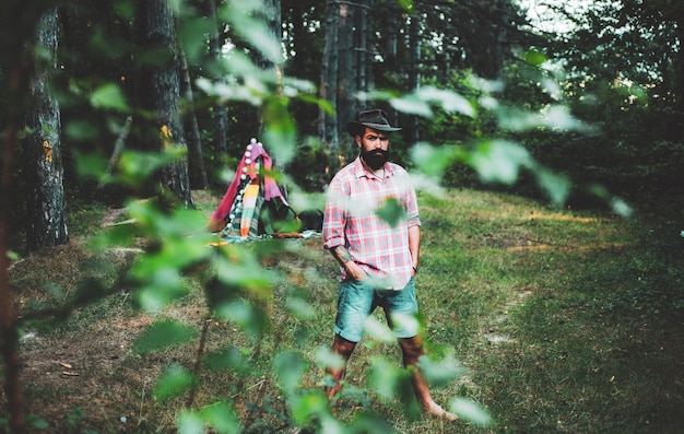 Hiking in deep wood Mature man with beard in hat Human and nature Masculinity and brutality conceptHipster tourist explore forest