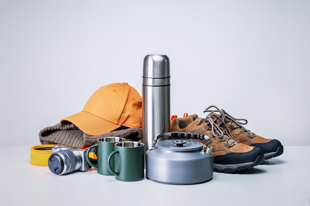 Фото Туристическое снаряжение, треккинговые ботинки, термос с камерой, чашки для одежды на сером столе