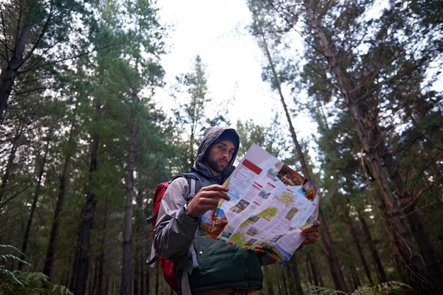 Foto escursioni in foresta e uomo ricerca mappa per la direzione per accamparsi in avventura nel bosco e lettura della navigazione viaggi confusi e persi nella natura trekking con zaino a spalla piano e guida alla posizione su carta