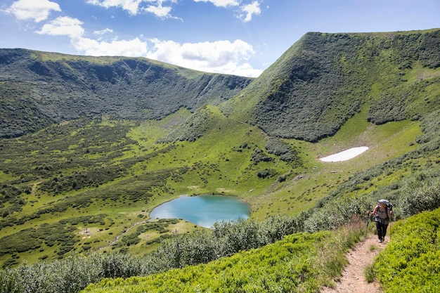 Hiking girl above the bowl of a mountain lake surrounded by forests and peaks