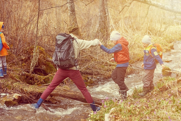 Hiking mother help children to cross mountain stream Sports family with backpacks