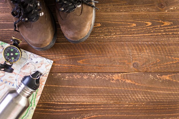 Походная обувь с топографической картой и компасом на деревянном фоне.