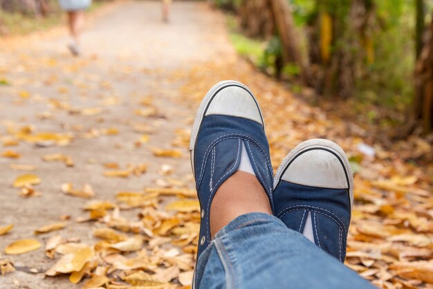 ハイキングシューズの若い女性の旅行者は夏の公園に座る。青いスニーカーの靴とジーンズの経路に焦点を当てる