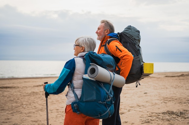 Photo hiking tourism adventure senior couple man woman enjoying outdoor recreation hiking on beach happy