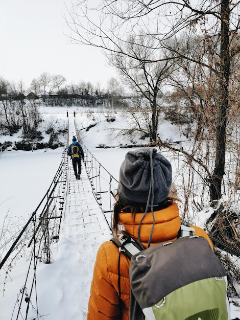 하이킹 관광객이 다리 겨울 보기와 함께 강 앞에 서 있다