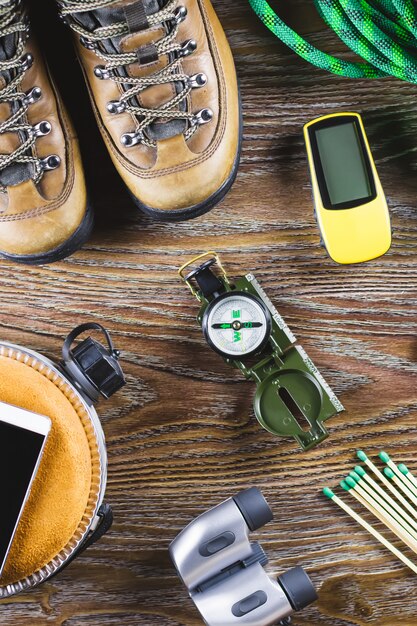 Hiking or travel equipment with boots, compass, binoculars, matches on woodentable. Active lifestyle concept