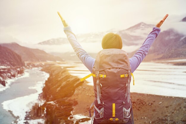 Hiking woman with a backpack at sunset raised her hands Beautiful young girl is traveling in the mountains