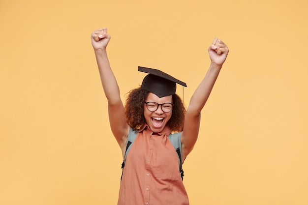 Foto hilarisch emotioneel afro-amerikaans studentenmeisje in academische pet die de ogen gesloten houdt terwijl ze haar succes viert