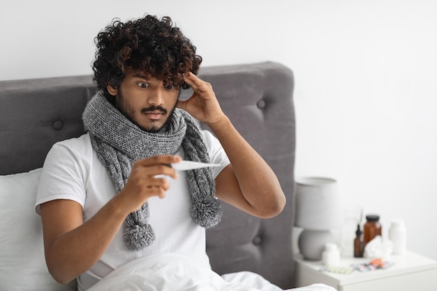 Индусский парень с шарфом на шее проверяет температуру тела