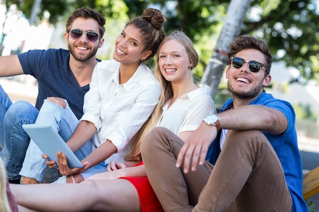 Hip friends holding tablet and sitting on sidewalk in the city