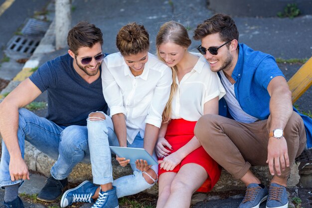 Hip friends looking at tablet and sitting on sidewalk in the city