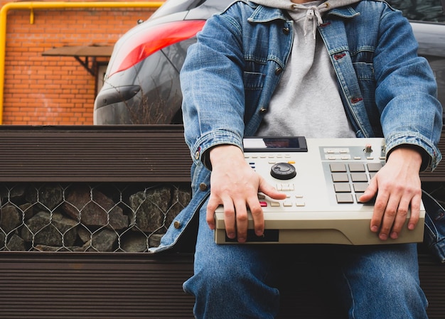 A hip hop beatmaker in the park holds an oldschool ' 90s drum machine in his hands Retro Digital Musical Instrument for Hip Hop Producers and Beatmakers