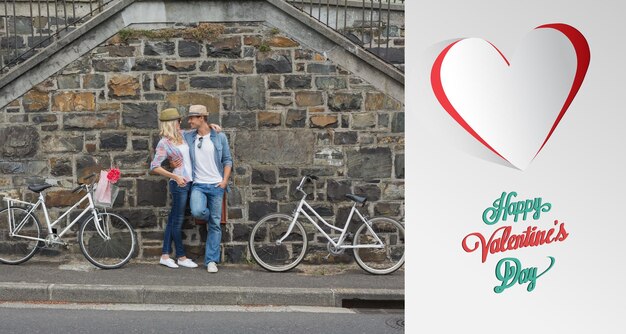 Foto anca giovane coppia in piedi accanto a un muro di mattoni con le loro biciclette contro il simpatico messaggio di san valentino