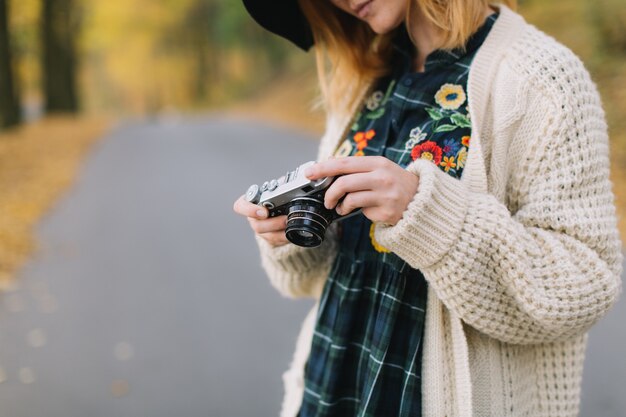 Hippie girl with old camera in a knitted sweater and hat walks autumn park.