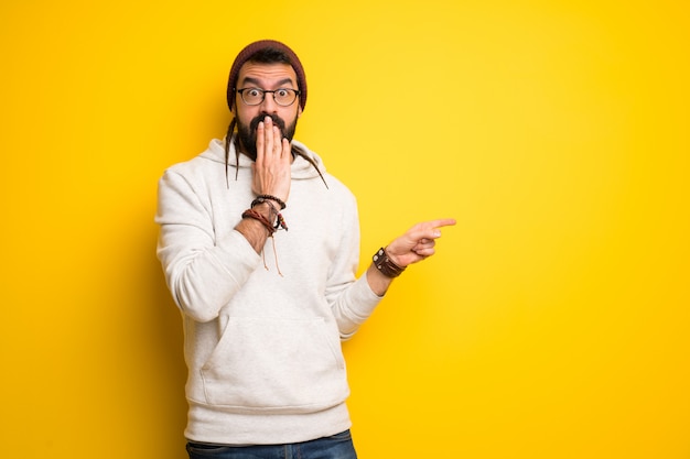 Hippie man with dreadlocks pointing finger to the side with a surprised face