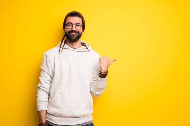 Hippie man with dreadlocks pointing to the side to present a product