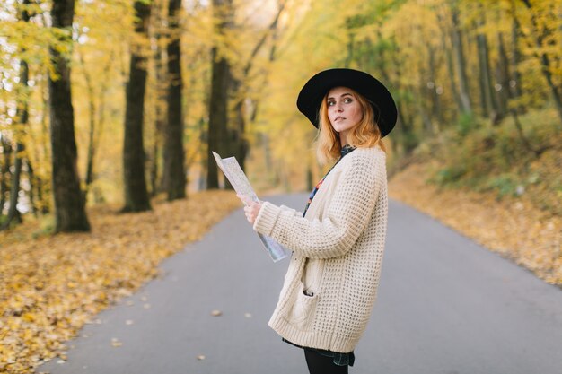 Hippie meisje met een kaart, oude camera in een gebreide trui en hoed wandelingen herfst park.