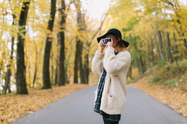 Hippie meisje met oude camera in een gebreide trui en hoed wandelingen herfst park.