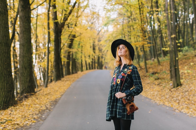 Hippie meisje met oude camera in een hoed loopt herfst park.