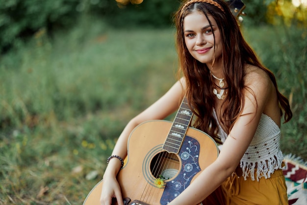 Hippie woman smiling and hugging her guitar in nature in the park in the sunset light High quality photo