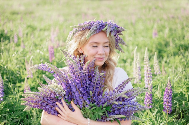 野花の花束を手に持ったヒッピーの女の子がルピナスの花束の後ろに顔を隠した