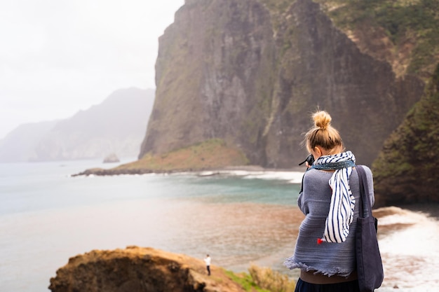 Hippy woman standing taking photos of the sea from a cliff