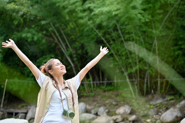 Hipster Asian female camper raises her hands taking a deep breath of the fresh air in the forest