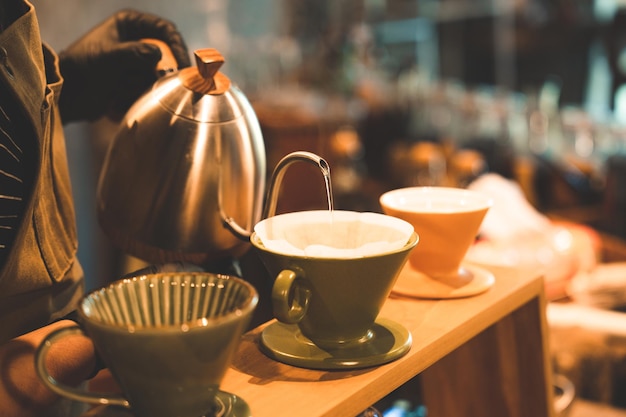 Hipster-barista die koffie drinkt met infuus- of filterstijl door heet water te gieten om een cafeïnedrank te brouwen van zwarte bonen in café-restaurantbedrijfswinkel met papier voor aroma in een kopje of mok