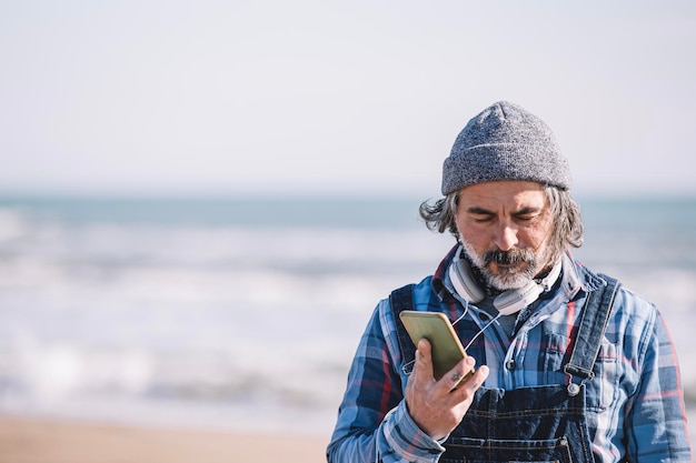 Hipster at the beach using a cell phone to send a voice message with the sea behind him