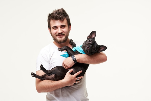 Hipster Bearded guy holding and hugging a nice French Bulldog dog in his arms with love and playing with him