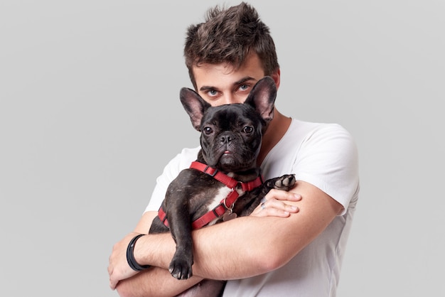 Hipster Bearded guy holding and hugging a nice French Bulldog dog in his arms with love and playing with him