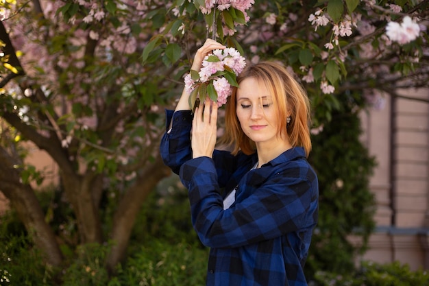 Hipster beautiful woman near sakura blooming tree Pink flowers spring and youth concept Stylish girl smiling