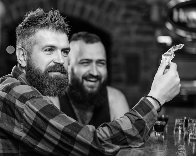 Hipster brutal bearded man spend leisure with friend at bar counter Men relaxing at bar Friendship and leisure Friday relaxation in bar Friends relaxing in pub Order drinks at bar counter