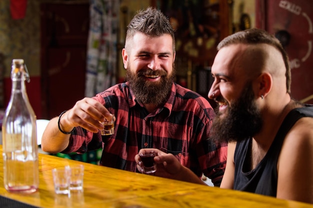 Uomo brutale hipster che beve alcolici con un amico al bancone del bar uomini ubriachi che si rilassano al pub divertendosi bevande alcoliche forti amici che si rilassano al pub uomini che bevono alcolici insieme dipendenza da alcol