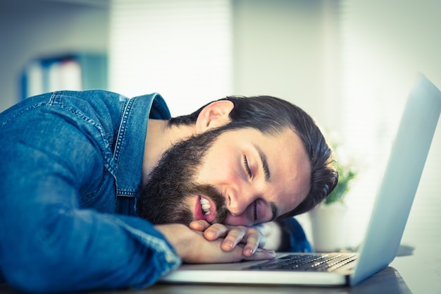 彼の机で眠っているヒップスターのビジネスマン