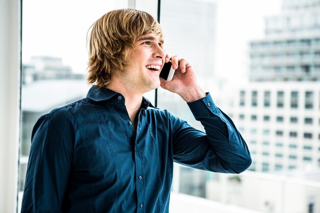 Uomo d'affari dei pantaloni a vita bassa che parla sul telefono contro la finestra