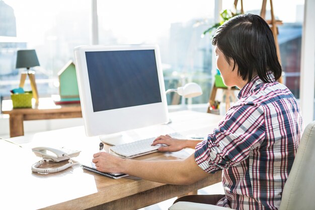 Hipster businessman using computer while writing in office 