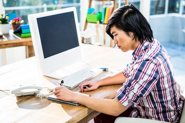 Hipster businessman writing on notebook in office