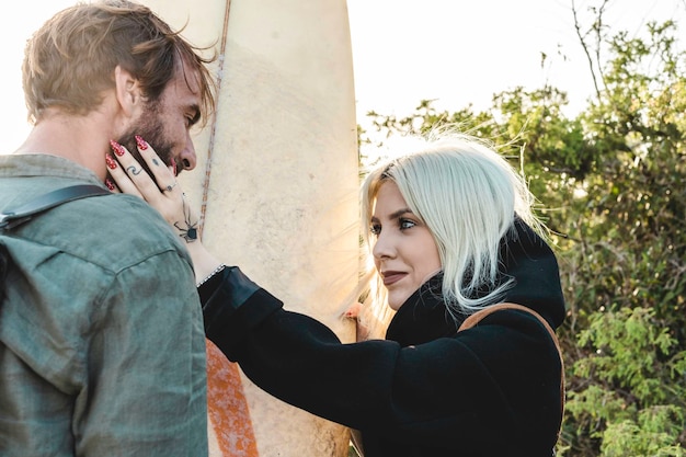 Hipster couple in love standing on wild dunes near the sea\
girlfriend caresses the boyfriend surfer with tattooed hand and\
looks him in the eyes black spider tattooed on girl hand lovers\
concept