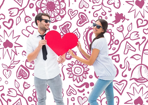 Photo hipster couple smiling at camera holding a heart against valentines pattern