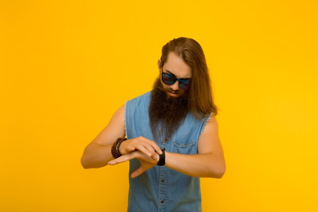 Hipster die de tijd op zijn polshorloge bekijkt tegen gele achtergrond.