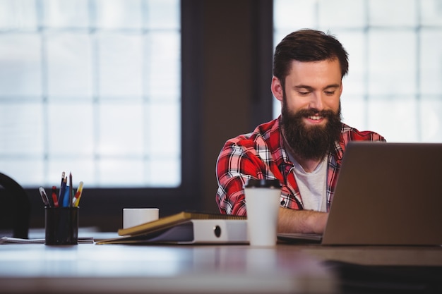 Hipster die terwijl het werken aan laptop glimlacht