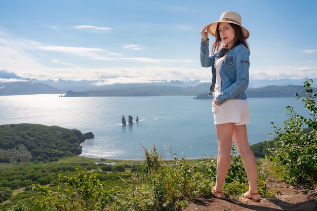 日当たりの良い夏の日にパノラマの海を背景に高い山に立っている流行に敏感な女性