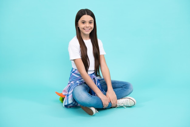 Hipster female teenager in trendy clothes Child girl with skateboard isolated on studio background Happy teenager positive and smiling emotions of teen girl