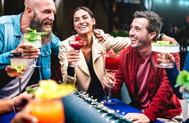 Amici hipster che tostano drink fantasiosi multicolori al fashion bar - persone alla moda che si divertono insieme a bere cocktail all'happy hour - concetto di tempo per feste di cibo e bevande su filtro a contrasto vivido