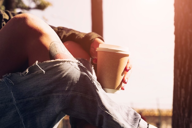 hipster getatoeëerd meisje zit in het park met koffie