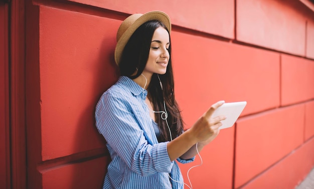 Hipster girl enjoying leisure time at urban setting for\
listening music via electronic headphones