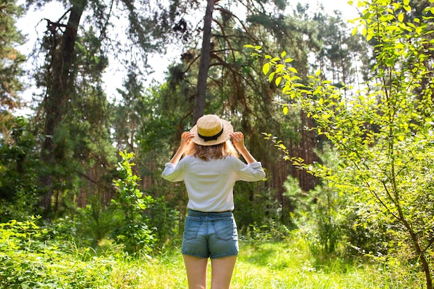 森の中に立つ麦わら帽子の内気な少女。ワンダーラストのコンセプト。旅行のアイデア。自然の中で美しい女性。夏のバイブス。